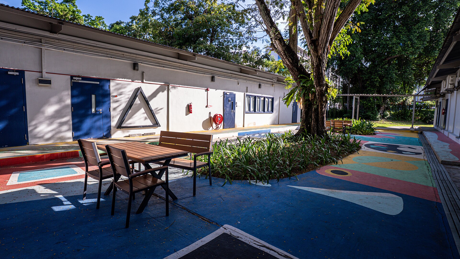 A colourful courtyard with tables and trees outside a block at Goodman Arts Centre